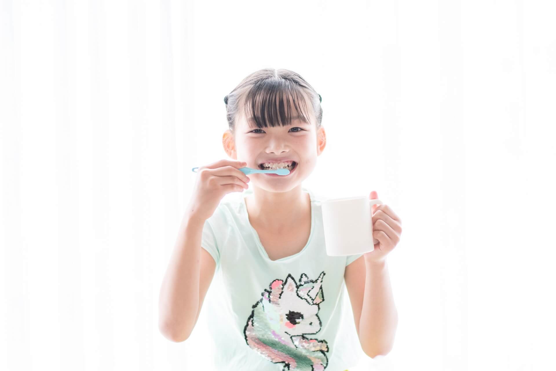 白い背景で歯を磨く微笑む少女